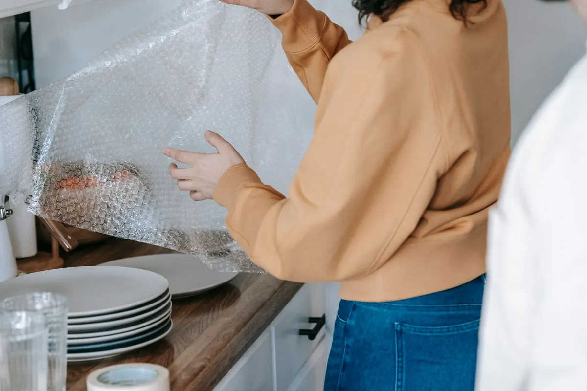 Mulher embalando pratos com plástico-bolha na cozinha