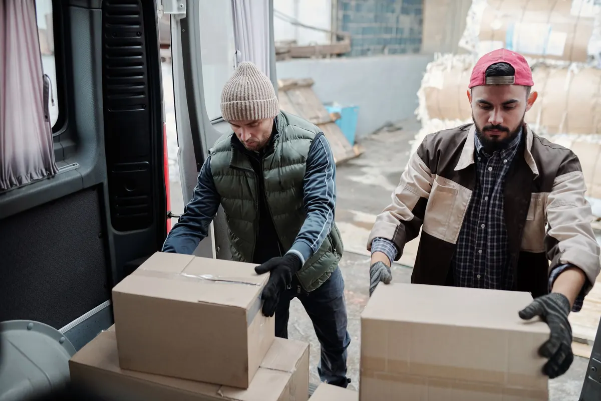 Dois carregadores colocando caixas dentro de uma van