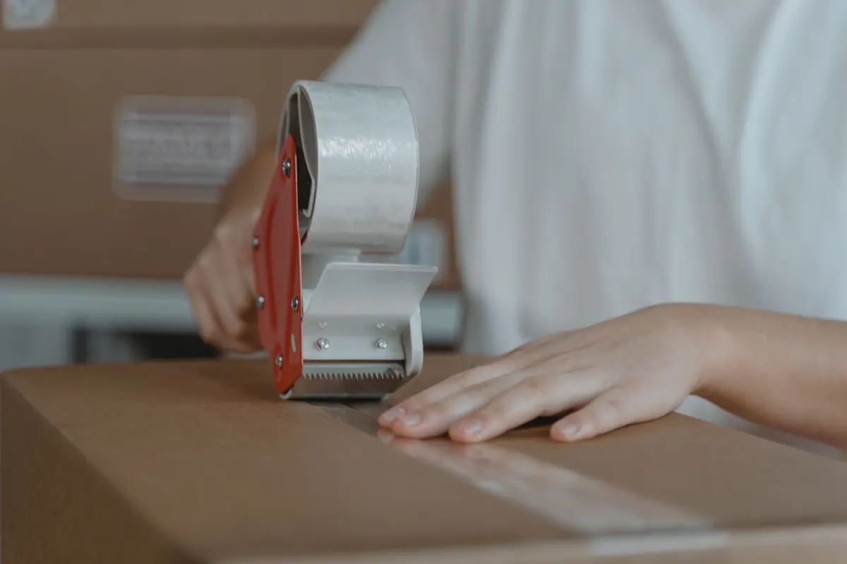 Pessoa fechando uma caixa de papelão com fita adesiva