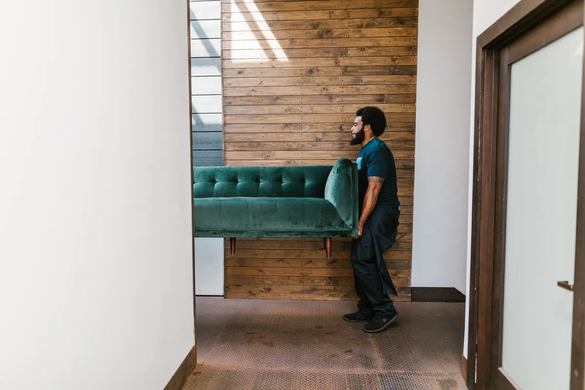 Carregador levando um sofá verde por um corredor